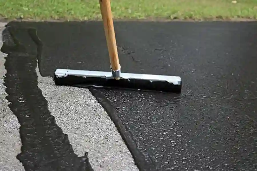 Applying asphalt sealant on pavement surface with a squeegee for waterproof protection.