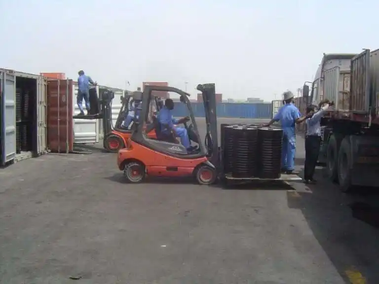 Workers loading bitumen drums into shipping containers using forklifts at ATDM facility.
